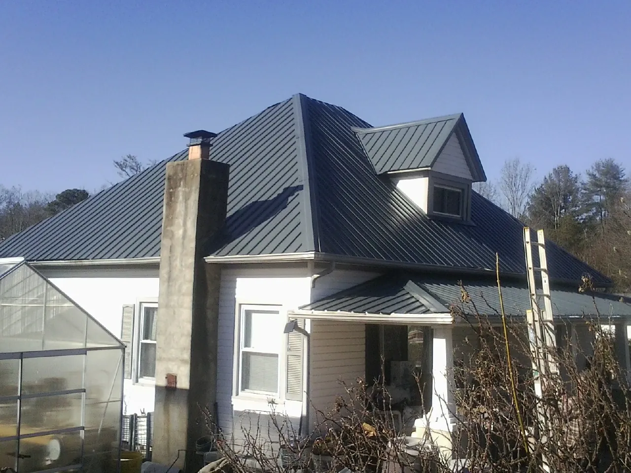 Dark blue standing seam metal roof on a white farmhouse with dormer — Slate & Tile Roof Repair by Roofing Brothers in Scottdale