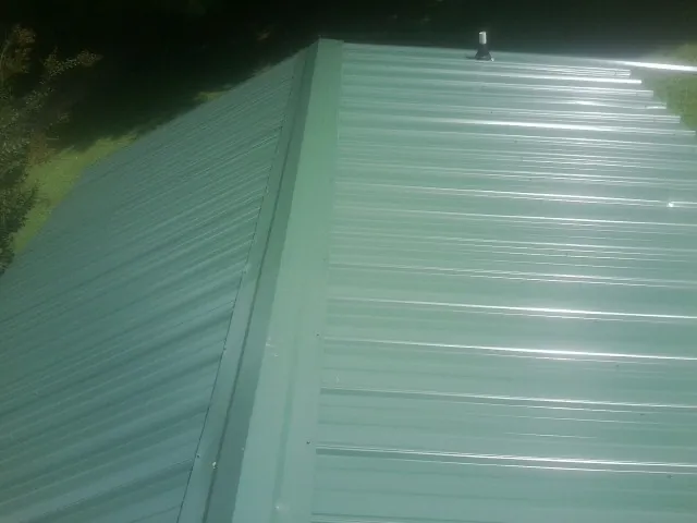 New green metal panels meeting at the ridge of a roof — Flat Roof Repair work by our crew in Scottdale