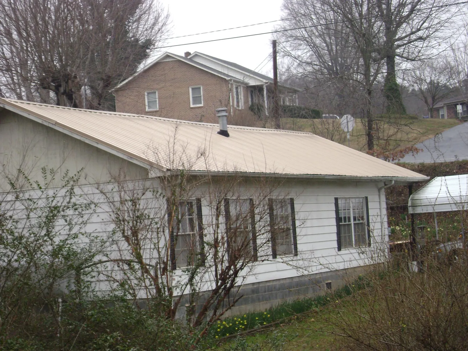 Tan metal roof on a white sided house set into a hillside — Commercial Roofing by Roofing Brothers in Scottdale